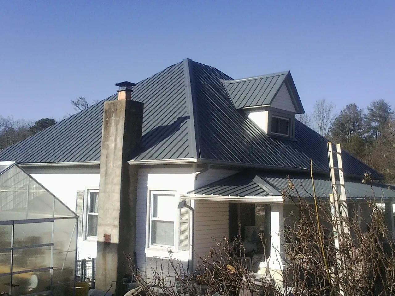 Dark blue standing seam metal roof on a white farmhouse with dormer — Slate & Tile Roof Repair by Roofing Brothers in Champlain