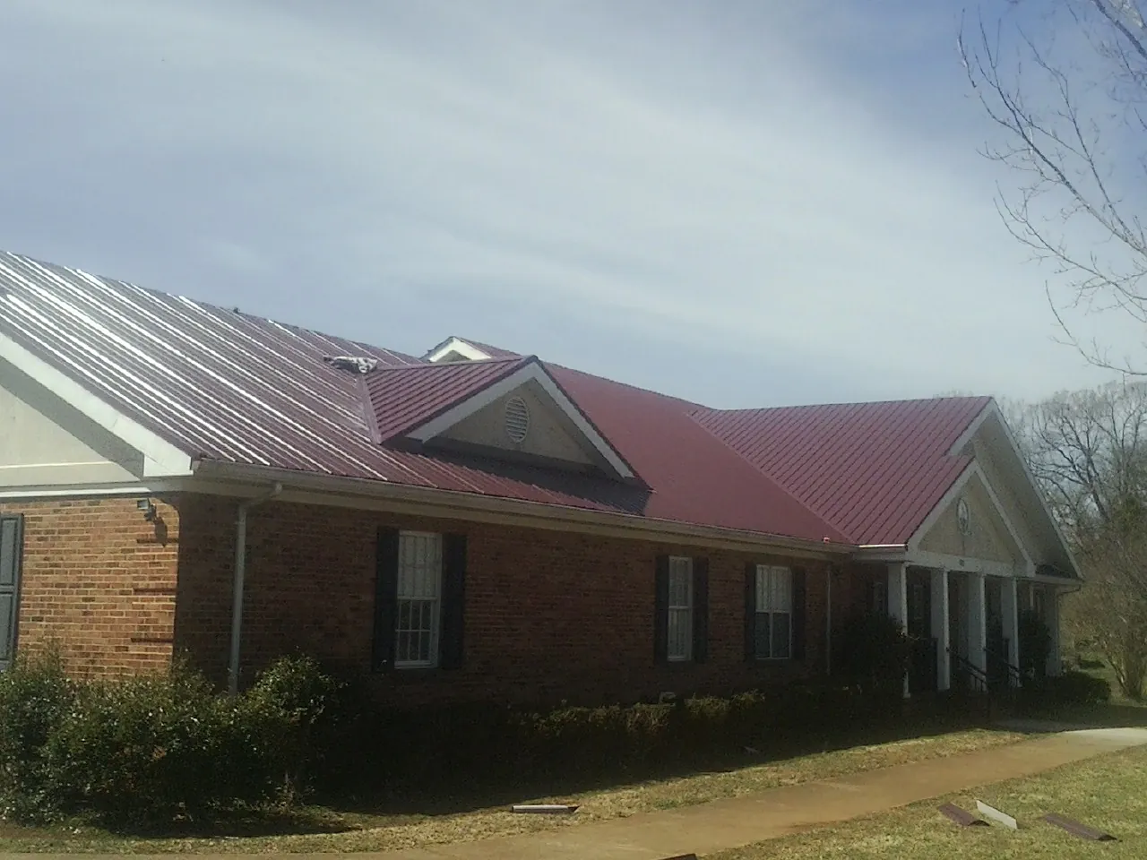 Red metal roof with gabled entries on a long brick building, from a Hail Damage Roof Repair job in Champlain