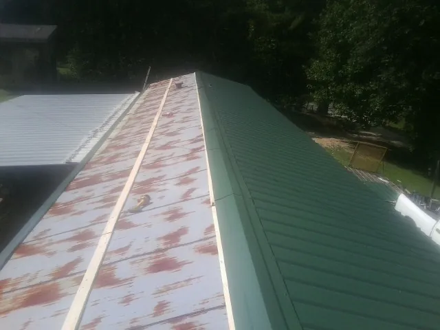 Old rusted panels beside newly installed green metal roofing — Wind Damage Roof Repair by Roofing Brothers in Champlain