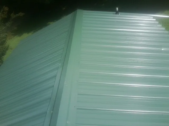 New green metal panels meeting at the ridge of a roof — Flat Roof Repair work by our crew in Champlain