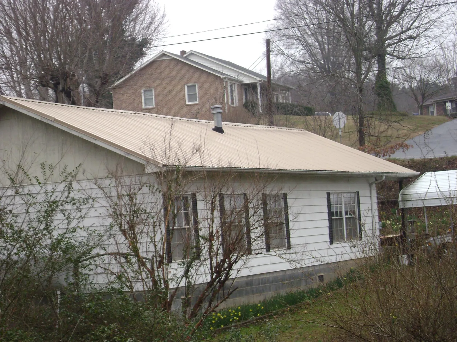 Tan metal roof on a white sided house set into a hillside — Commercial Roofing by Roofing Brothers in Champlain