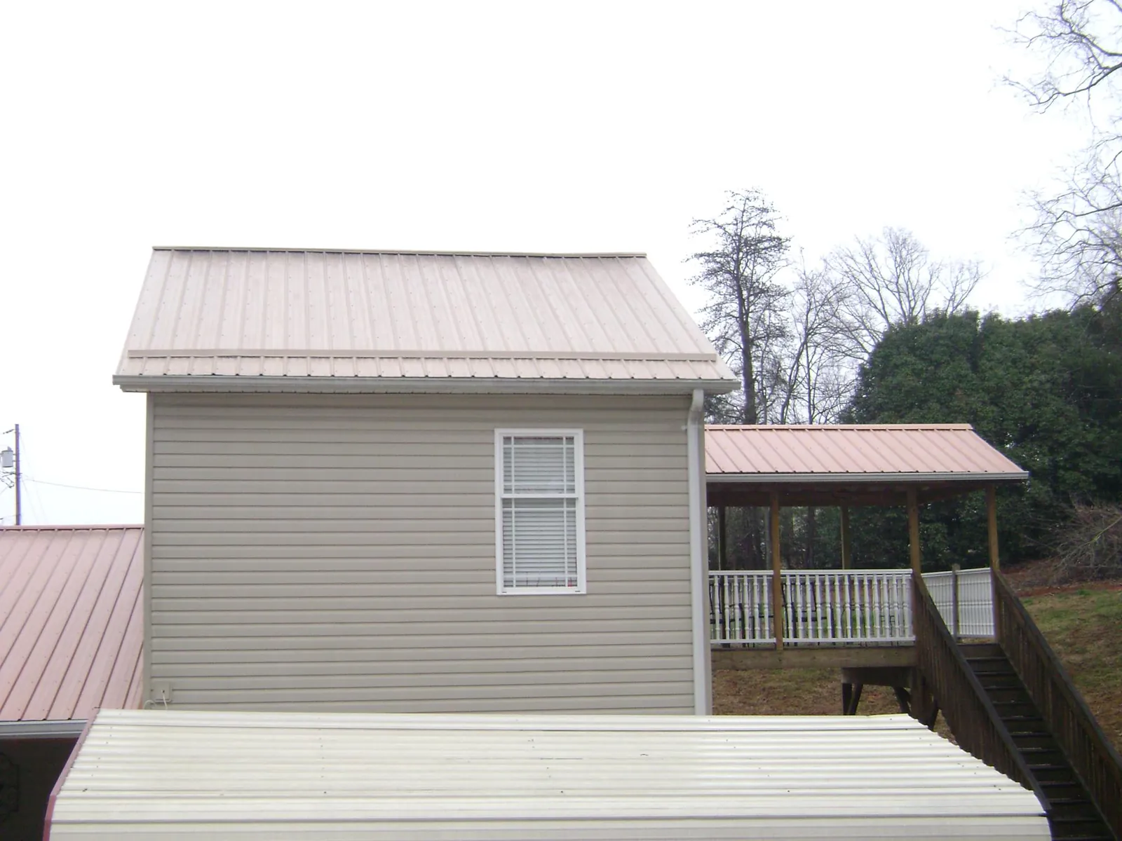 Tan metal roofs on a two story addition and attached porch, from a Roof Replacement job in Champlain